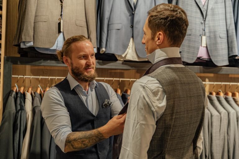 Tailor assists customer in clothing store with suit fitting. Professional attire and tailoring service.
